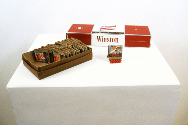 THE TRICK IS, THERE IS NO “K” <br/>
1998 Ongoing <br/>
Vintage Matchbooks from the Collect All Game with Letters that Potentially Spell the Name “Dikeou,” a Carton of Cigarettes, Podium <br/>
Variable Dimensions<br/>