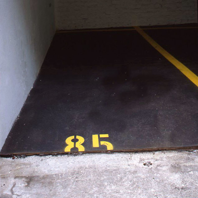 “ASPHALT JUNGLE”: PAY HERE; KOLN<br />
1991 Ongoing<br />
Floor: Asphalt Installed on Top of Gallery Floor to Create Sections of 12 Spaces of an Abstract 100 Space Parking Lot‚ Parking Lines‚ and Numbers Painted on Asphalt to Delineate Parking Spaces<br />
Detail: Spaces 85, 86, 95, 96<br />
Regulation Standard Parking Spaces<br />
Variable Dimensions<br />
