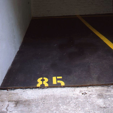 “ASPHALT JUNGLE”: PAY HERE; KOLN<br />
1991 Ongoing<br />
Floor: Asphalt Installed on Top of Gallery Floor to Create Sections of 12 Spaces of an Abstract 100 Space Parking Lot‚ Parking Lines‚ and Numbers Painted on Asphalt to Delineate Parking Spaces<br />
Detail: Spaces 85, 86, 95, 96<br />
Regulation Standard Parking Spaces<br />
Variable Dimensions<br />