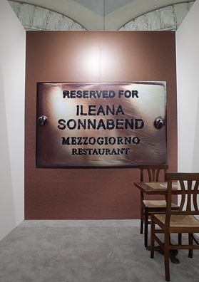 RESERVED FOR ILEANA SONNABEND: “BUDDHA OR MACHIAVELLI” <br />
(Brenda Richardson about Ileana Sonnabend as quoted by Calvin Tomkins— <i>The New Yorker</i>)<br />
2010 Ongoing<br/>
Close Up View<br />
Wall: C-Print of Name Plate Reserving a Table in Perpetuity for the Preeminent Art Dealer Ileana Sonnabend<br />
Floor: 1 Table and 2 Chairs from the Restaurant Mezzogiorno<br />
Variable Dimensions<br />