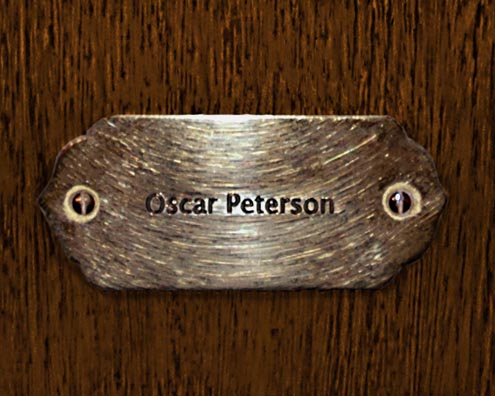 “MAMAS DON'T LET YOUR BABIES GROW UP TO BE COWBOYS”<br/>
Oscar Peterson<br/>
2009 ongoing <br/>
C-Print of a Name Plate Reserving a Hotel Room in Perpetuity for the Piano Jazz Legend, Oscar Peterson<br/>
Mounted on Wood with Non-Glare Plexiglas Surface<br/>
7 3/4” x 9 3/4” x 3/4” <br/>