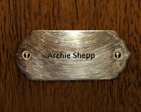 “MAMAS DON'T LET YOUR BABIES GROW UP TO BE COWBOYS”<br/>
Archie Shepp<br/>
2009 ongoing <br/>
C-Print of a Name Plate Reserving a Hotel Room in Perpetuity for the Multifarious Jazz Legend, Archie Shepp<br/>
Mounted on Wood with Non-Glare Plexiglas Surface<br/>
7 3/4” x 9 3/4” x 3/4” <br/>