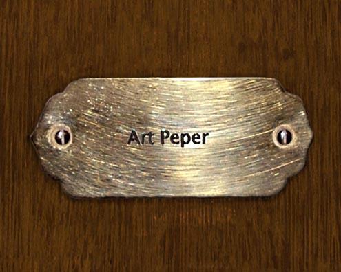 “MAMAS DON'T LET YOUR BABIES GROW UP TO BE COWBOYS”<br/>
Art Peper [Sic]<br/>
2009 ongoing <br/>
C-Print of a Name Plate Reserving a Hotel Room in Perpetuity for the Alto Sax Jazz Legend, Art Pepper<br/>
Mounted on Wood with Non-Glare Plexiglas Surface<br/>
7 3/4” x 9 3/4” x 3/4” <br/>