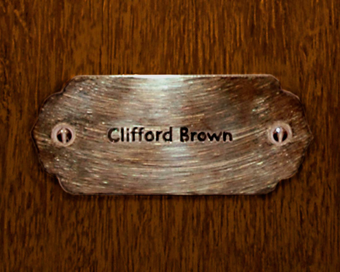“MAMAS DON'T LET YOUR BABIES GROW UP TO BE COWBOYS”<br/>
Clifford Brown<br/>
2009 ongoing <br/>
C-Print of a Name Plate Reserving a Hotel Room in Perpetuity for the Trumpet Jazz Legend, Clifford Brown<br/>
Mounted on Wood with Non-Glare Plexiglas Surface<br/>
7 3/4” x 9 3/4” x 3/4” <br/>