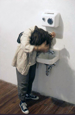 “COME YOU SPIRITS, WHICH TEND ON MORTAL THOUGHTS” - <i> Macbeth, </i> Shakespeare<br />
1993 Ongoing<br />
Happening: Functioning Kohler Sink, Soap Dispenser, and Air Dryer Installed in Gallery and Being Used by Les Ayre to Dry Her Hair<br />
Photograph of Happening <br />
Variable Dimensions<br />