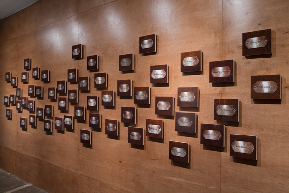 “MAMAS DON'T LET YOUR BABIES GROW UP TO BE COWBOYS”<br/>
2009 ongoing <br/>
Lateral View<br/>
Wall: 56 C-Prints of Name Plates Reserving Hotel Rooms in Perpetuity for 56 Jazz Legends Mounted on Wood with Non-Glare Plexiglas Surface and Installed on a Wall of Wood Paneling<br/>
C-Prints: 7 3/4” x 9 3/4” x 3/4” Each<br/>