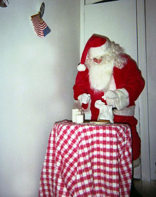 “YOU BETTER WATCH OUT”<br />
1991 Ongoing<br />
Happening: Professional Santa Claus Asking Viewers‚ “If They Have Been Bad or Good”‚ and Delighting in Milk and Cookies Left by the Artist for Santa to Devour<br />
Photograph of Happening: “Santa Baby” Looking to Spike the Eggnog<br />